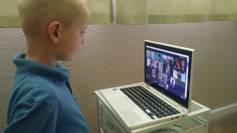 A boy gazes at a laptop showing his elementary school class.