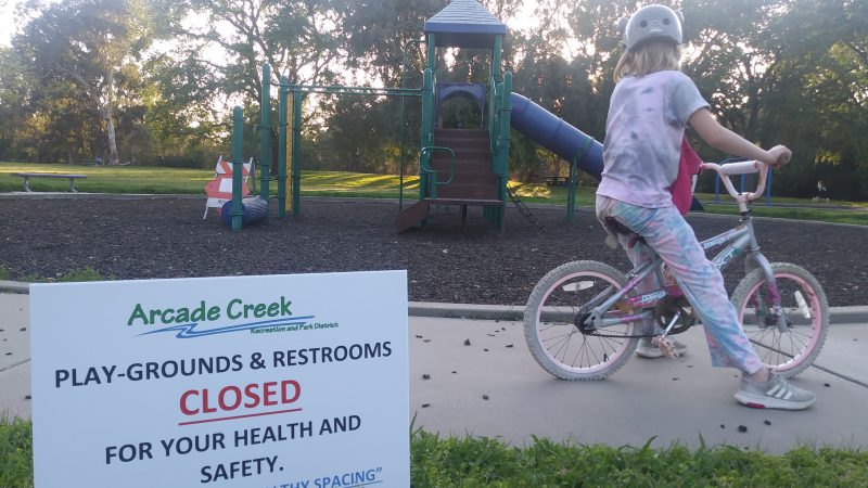 A girl on a bicycle stares at a closed playground.