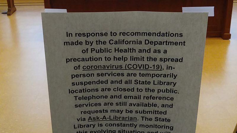 A sign is taped to a circular window on a door leading into a library reading room.