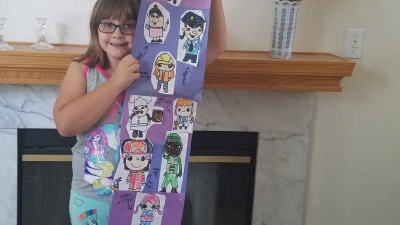 A young girl holds up a handmade purple mural featuring pictures of doctors, nurses, police officers and other frontline workers.