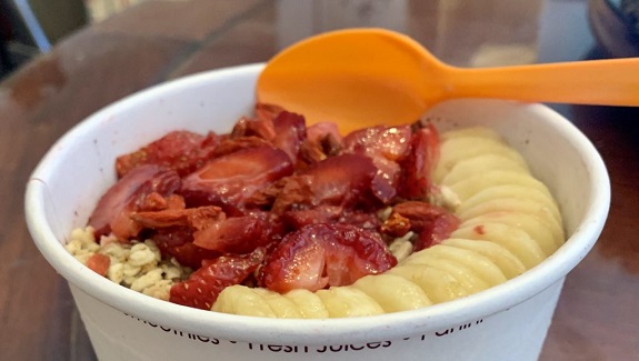 A white paper cup of strawberries, bananas and granola with the label "Vitality Bowls Superfood Cafe."