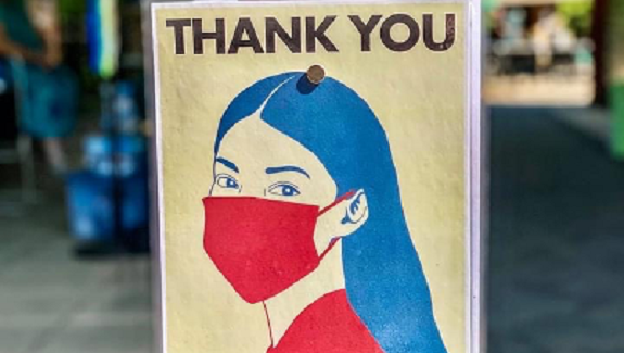 A sign featuring the words "Thank You" above a blue and red image of a woman wearing a face mask.