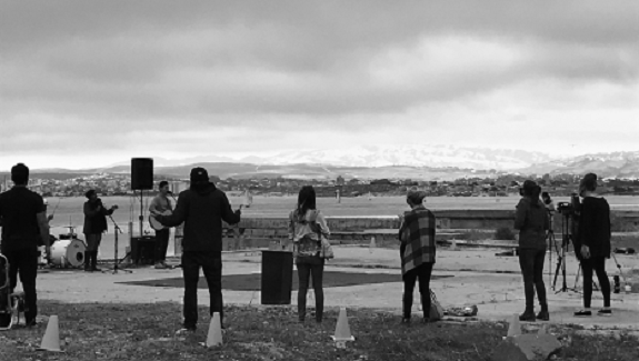 A black and white of eight people standing in a circle on a cloudy day, with mountains in the background.