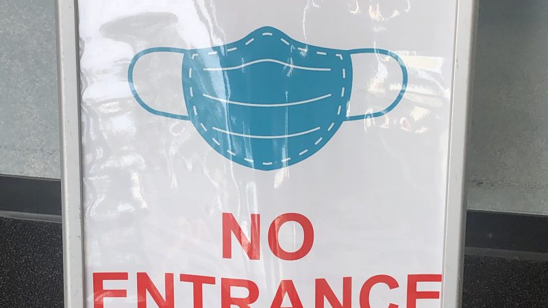 A sign reads "NO MASK NO ENTRANCE" in red letters with an image of a face mask.