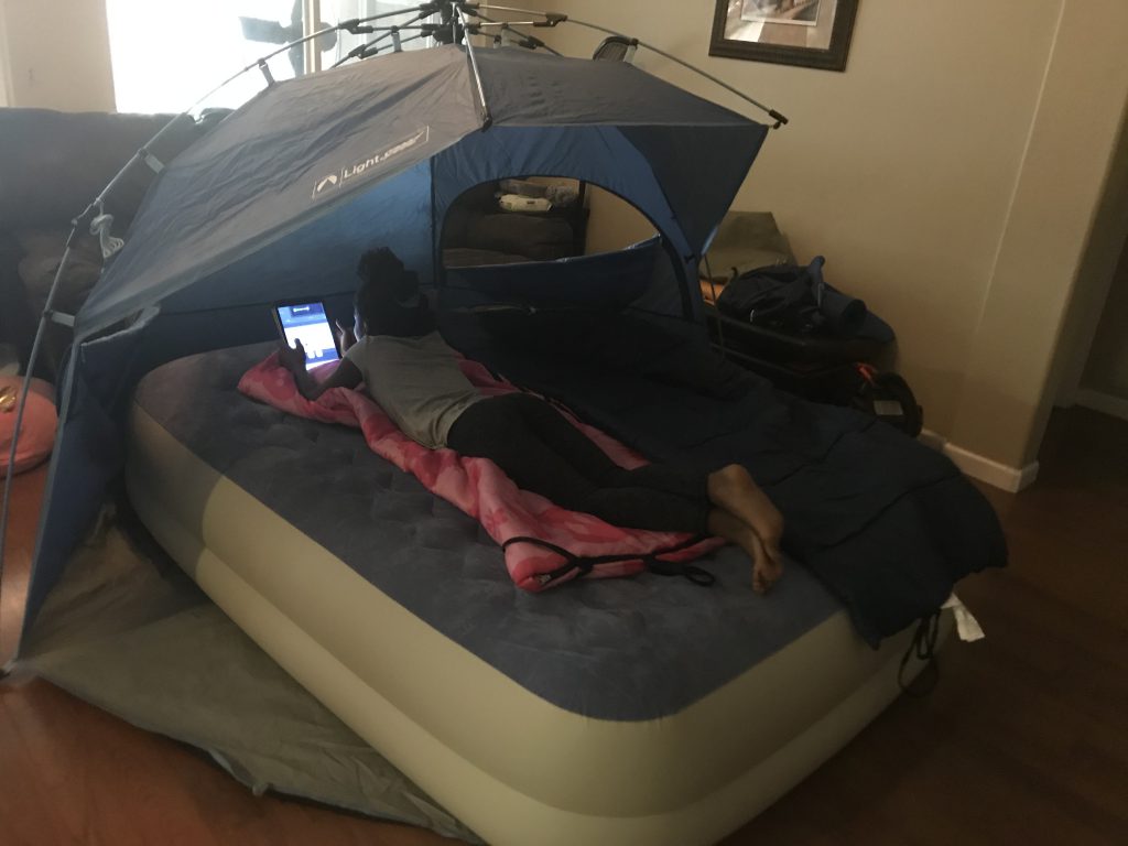 Young girl laying on an air mattress looking at her ipad, while indoor camping.