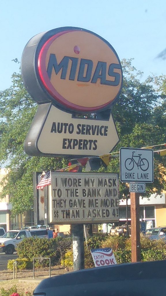 A sign outside a Midas Auto Service business surrounded by trees.