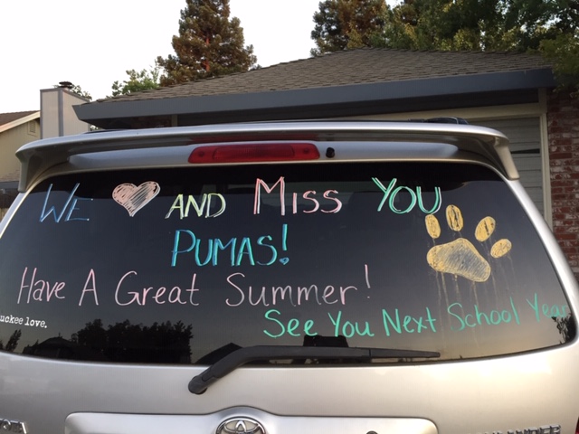 Handwritten messages in blue, green, yellow and pink are visible on the back window of a gray SUV.