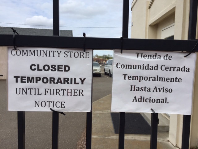 Two black and white signs attached to a black iron fence with vehicles visible in the parking lot behind.