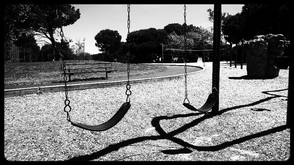 A black and white photograph of an empty swingset in a playground.