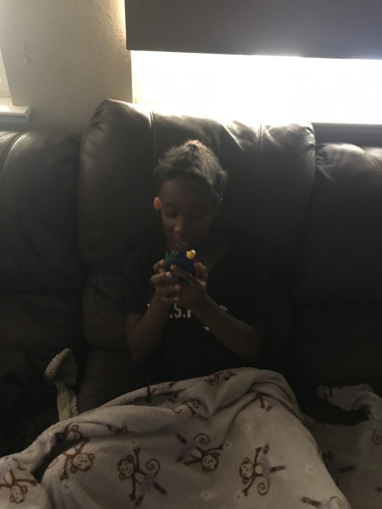 A young girl in a black t-shirt sits on a large leather sofa and speaks into a walkie-talkie.