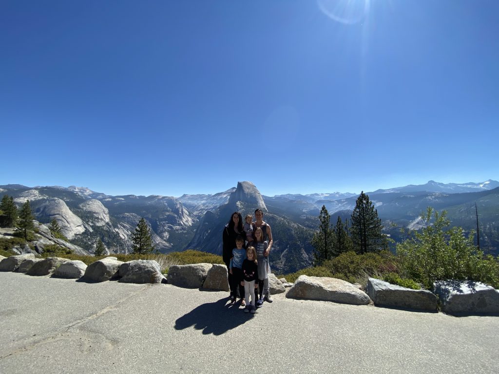 A man, woman and three children standing in front of a mountain range on a clear, sunny day.