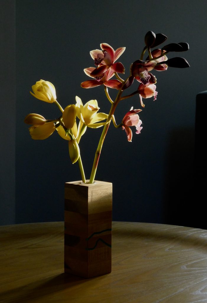 Two orchids in a wooden vase on a table.