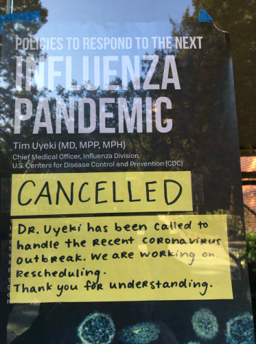 A sign in a window reading "Policies to Respond to the Next Influenza Pandemic" has a "CANCELLED" sign on top of it.