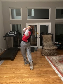 A person is swinging a golf club inside a house.